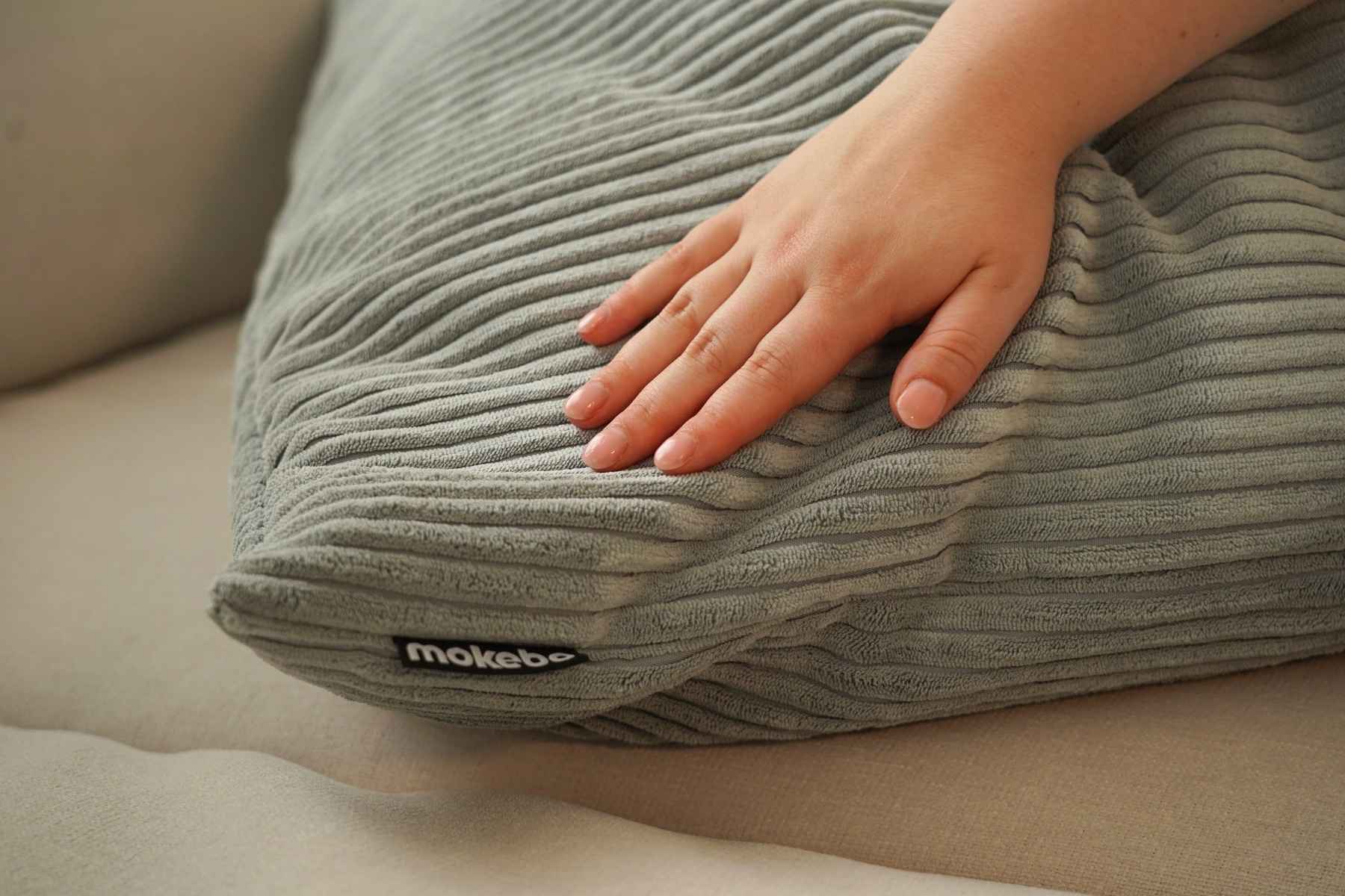 Coussin côtelé gris clair. Main caressant le coussin.