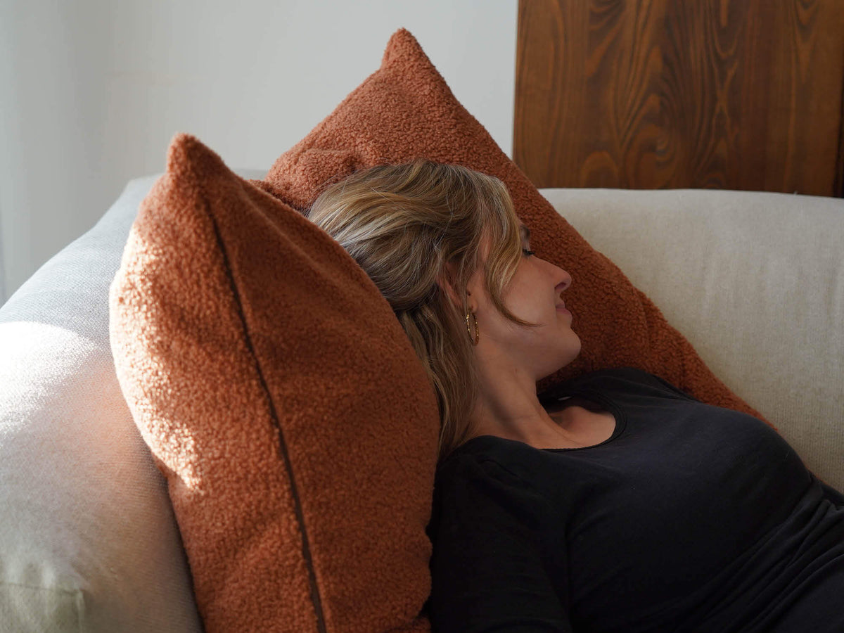 Großes XXL Kissen aus Bouclé 'Hug' auf einem Sofa, Frau liegt mit dem Kopf auf dem Kissen und schläft