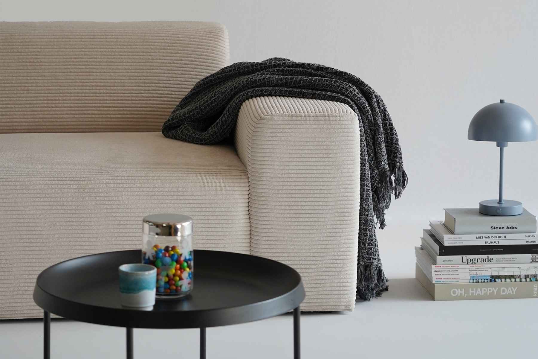Canapé en velours côtelé beige avec une couverture draped sur l'accoudoir droit
