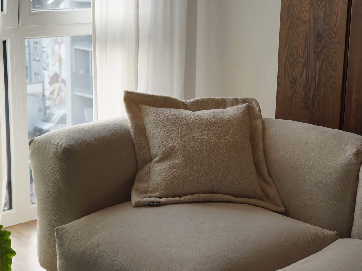 Bouclé Sofakissen 'Laze' in beige auf einem Sofa 