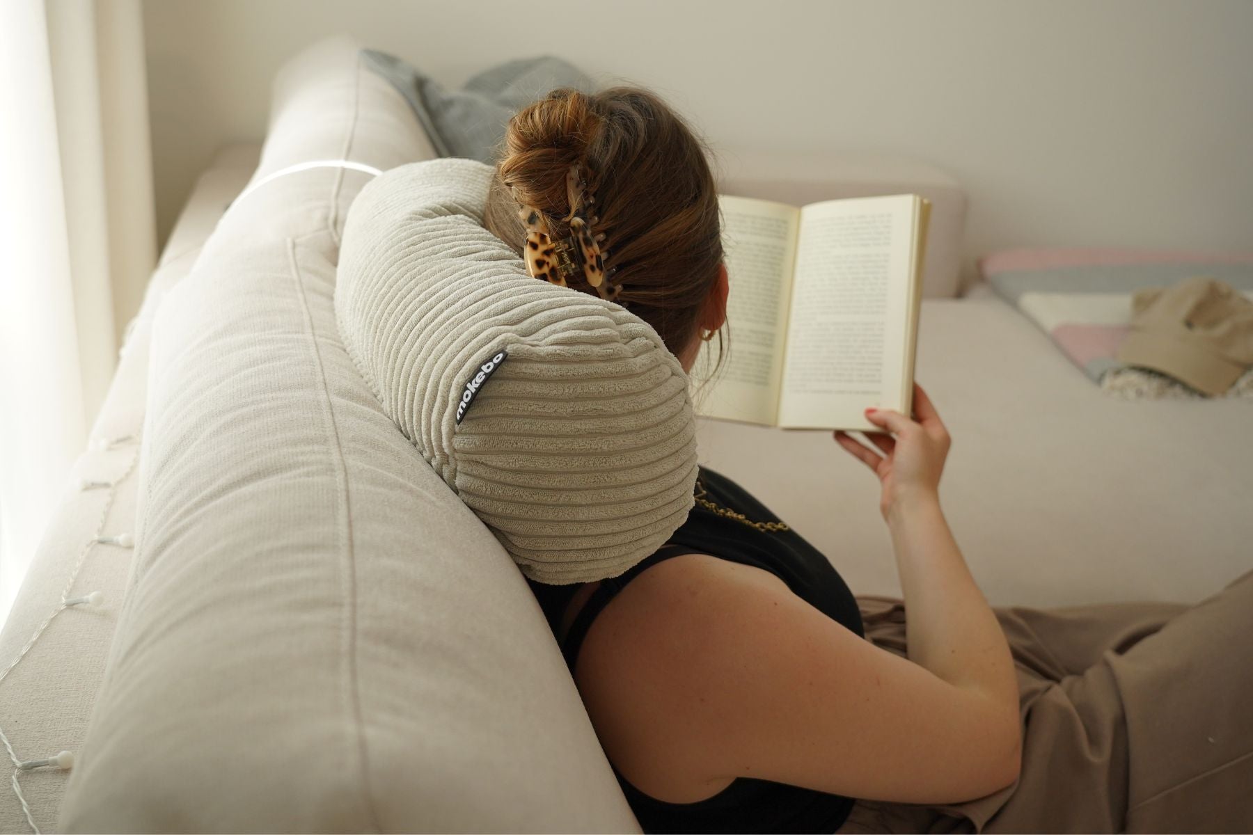 Oreiller cervical en velours côtelé beige. L'oreiller est placé au cou d'une femme. La femme lit et regarde loin de la caméra.
